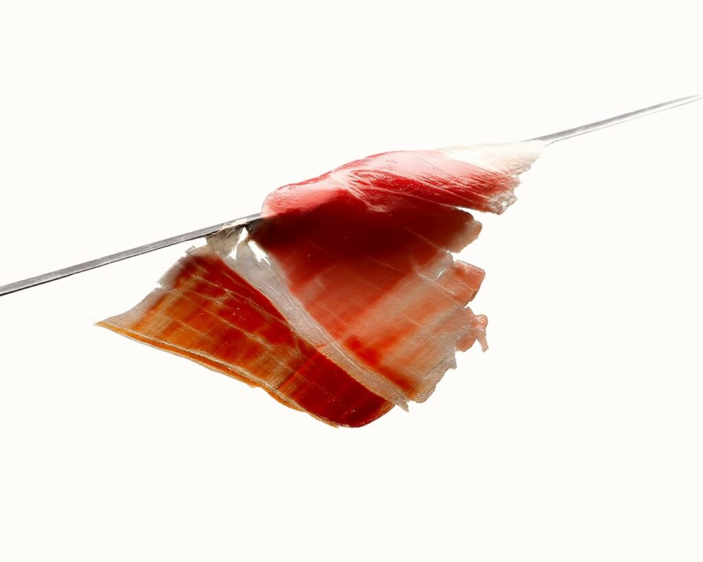 Loncha de jamón ibérico finísima, casi transparente, lisa y elegante sobre el cuchillo