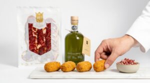 Croquetas de jamón ibérico recién hechas sobre mármol blanco, con el sobre de loncheado de jamón RH Gourmet y la botella de aceite de oliva virgen extra RH Gourmet al fondo