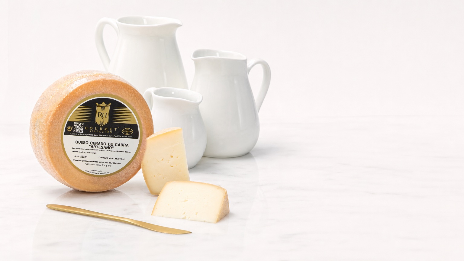 Queso curado de cabra RH con cuñas sobre mármol blanco y tres jarras de leche al fondo